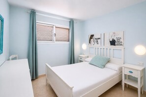 Een slaapkamer met een bed, nachtkastje, gordijnen en decoratieve wandkunst.