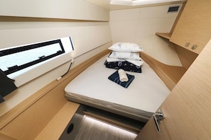 Ein kleines Zimmer mit Bett, Fenster und einer kleinen Ablagefläche.