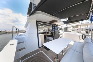 Eine Terrasse im Freien mit einem weißen Tisch, einer Sitzecke, einer kleinen Küche und Blick auf den Hafen.