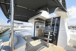 Un espacio al aire libre cubierto con una zona de estar, un vidrio que da a un espacio interior y vistas al puerto deportivo de fondo.