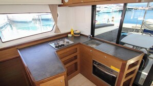 A compact kitchen with a stove, sink, and oven, wooden cabinetry, and a view of the marina through a large window. - Sun-Kissed Sailing Adventure in Split, Croatia (Split)