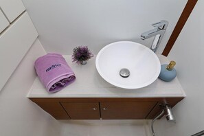 Ein Badezimmer mit einem weißen Waschbecken, einem violetten Handtuch, einer kleinen Topfpflanze und einem blauen Seifenspender.