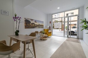Eine Hotelhalle mit einer Rezeption, Stühlen, einem Tisch, einem großen Fenster und einem Gemälde an der Wand.