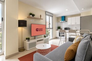 Een moderne woonkamer met een flatscreen televisie waarop 'GUEST READY' staat, een bank, een salontafel en een rood vloerkleed.
