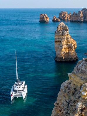 A sailboat anchored near a rocky coastline with clear blue waters.