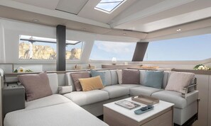 A modern yacht interior with a curved sofa, a coffee table, and large windows offering a view of the sea.