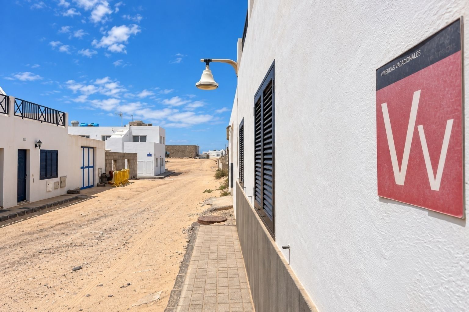 Une rue étroite bordée de bâtiments blancs, un ciel dégagé et une enseigne indiquant « WIVENDAS VACACIONALES ».