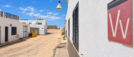 Une rue étroite bordée de bâtiments blancs, un ciel dégagé et une enseigne indiquant « WIVENDAS VACACIONALES ».
