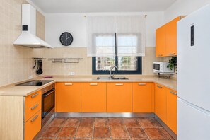 Een keuken met oranje kastjes, een witte kookplaat, een magnetron en een klok aan de muur.