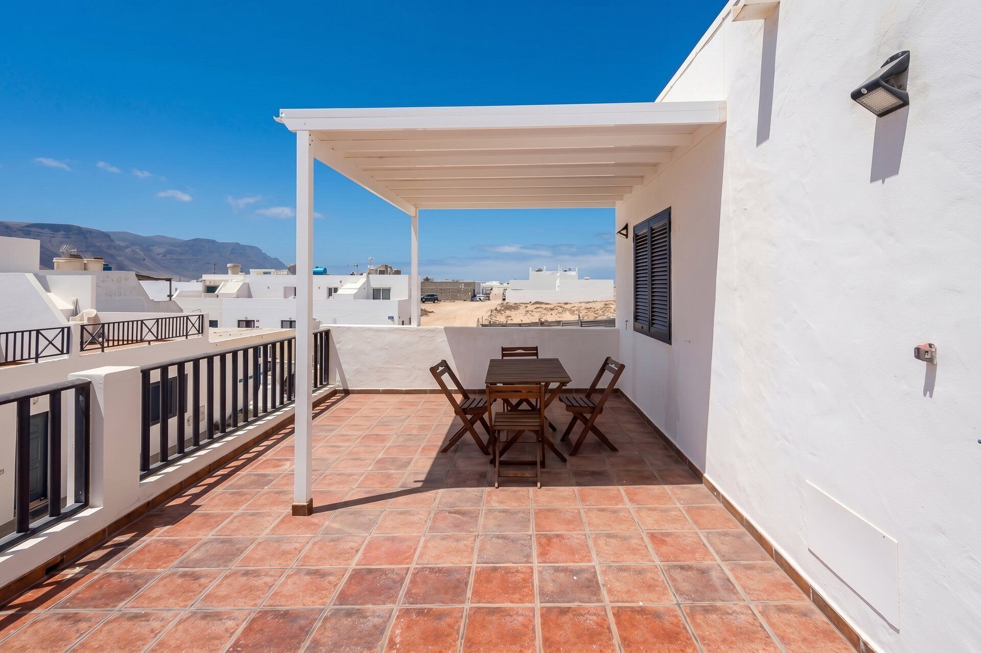 Une terrasse sur le toit, avec une table et des chaises, des murs blancs et une vue sur la mer et les montagnes.