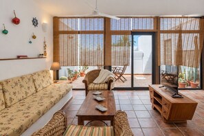 A living room with a sofa, a coffee table, a wicker chair, and a television. - GuestReady - La Graciosa Natural Paradise (Caleta de Sebo)