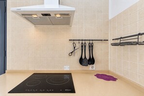 A kitchen with a built-in induction cooktop, a white range hood, and hanging kitchen utensils. - GuestReady - La Graciosa Natural Paradise (Caleta de Sebo)