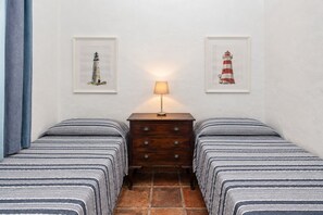 Ein Zimmer mit zwei Betten, einem Nachttisch mit Lampe und zwei gerahmten Bildern von Leuchttürmen an der Wand.