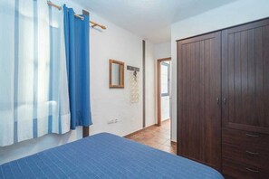 Un dormitori amb llit, armari, mirall i una porta que dona a una altra habitació.