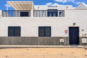 Een gebouw met twee verdiepingen, een witte gevel, een blauwe deur en een balkon met een hekwerk.