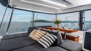 Interieur van een jacht met een bank, kussens, een houten tafel en een bloevas.