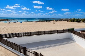 A beach with a fenced swimming area and a clear view of the ocean. - GuestReady - Cosy Retreat with Balcony near Beach (El Cotillo)