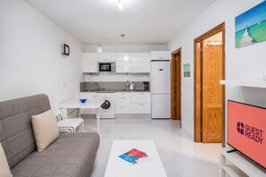 Ein kompakter Wohnraum mit Küchenzeile, einer Couch, einem Essbereich und einem Fernseher.