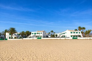 A beachfront property with multiple white buildings, palm trees, and a sandy beach. - GuestReady - Cosy Retreat with Balcony near Beach (El Cotillo)