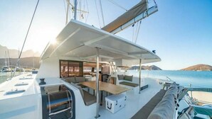 Eine Yacht mit überdectem Deck, Sitzgelegenheiten und Blick auf Wasser und Berge.