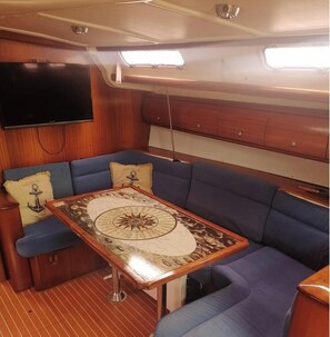 Uma cabana com teto de madeira, uma televisão presa na parede, uma mesa redonda com design de bússola e assentos estofados azuis.