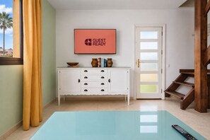 Une pièce avec un meuble blanc, un téléviseur à écran plat, une télécommande et un escalier en bois.