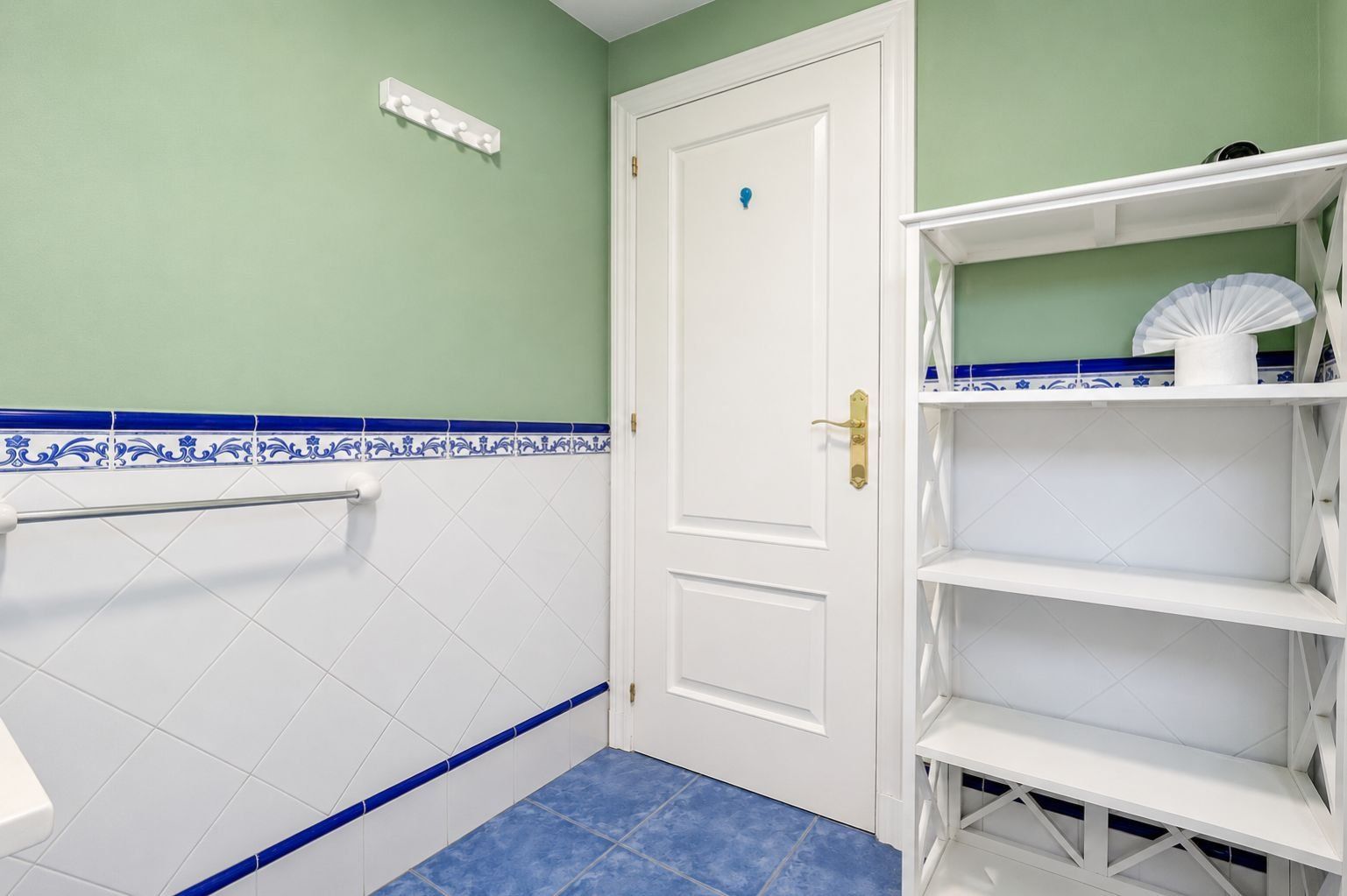 Une salle de bain avec une porte blanche, un porte-serviettes et une étagère sur laquelle se trouve un ventilateur.