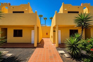 Une cour bordée de bâtiments jaunes, un chemin pavé et quelques espaces verts.