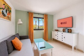 Un salon moderne avec un canapé, une table basse en verre, un meuble blanc et un téléviseur affichant le message « PRÊT POUR LES INVITÉS ».