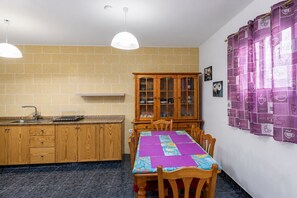 A kitchen with wooden cabinets, a dining table with chairs, a hanging pendant light, and a cabinet with glass doors. - GuestReady - Gadi House Rural Retreat (Tasarte)