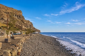 Ein felsiger Strand, bewölkter Himmel, ein geparkter Wagen und ein Gebäude mit geneigtem Dach.