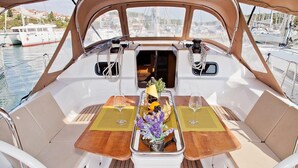 Ein Bootsdeck mit Tisch für zwei Personen, einem kleinen Fenster und Blick auf den Hafen.
