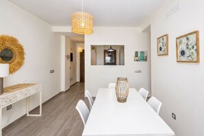 Ett modernt matområde med ett vitt bord, stolar, en hängande lampa och inramade konstverk på väggen.