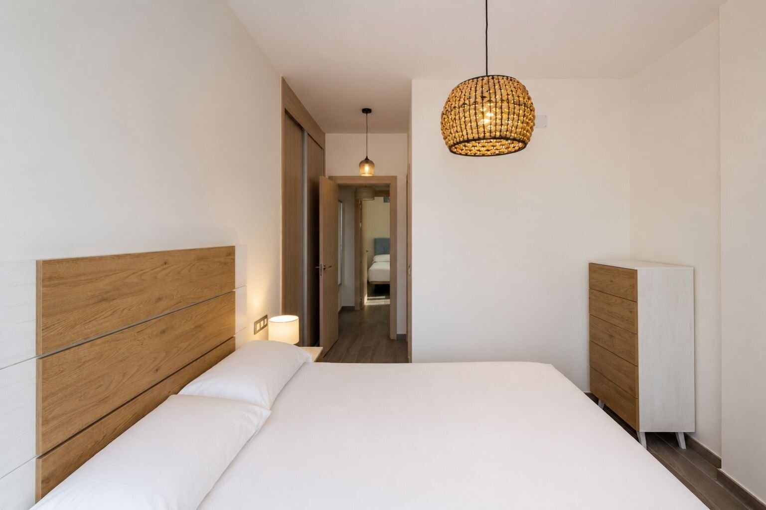 Ein modernes Hotelzimmer mit einem großen Bett, einem Holzkopfteil, einer Nachttischlampe und einer Pendelleuchte.