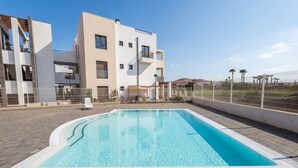 A modern building with a swimming pool, outdoor seating, and a fenced area. - GuestReady - Pueblo Majorero Sunny Stay and Pool (Antigua)
