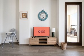Ein Zimmer mit einem Holz-Fernsehmöbel, einer Wanduhr, einem gerahmten Bild und einem Korbwäschesammler.
