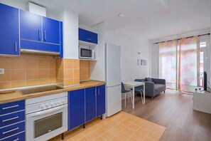 Une cuisine compacte avec des meubles bleus, un four à micro-ondes, un réfrigérateur et un coin repas comprenant une table et des chaises.