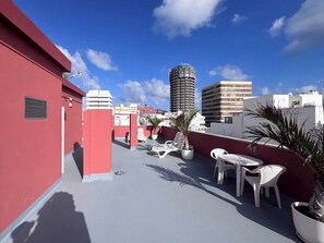 Une terrasse sur le toit, dotée de chaises longues blanches, de plantes en pot et offrant une vue dégagée sur les bâtiments environnants.