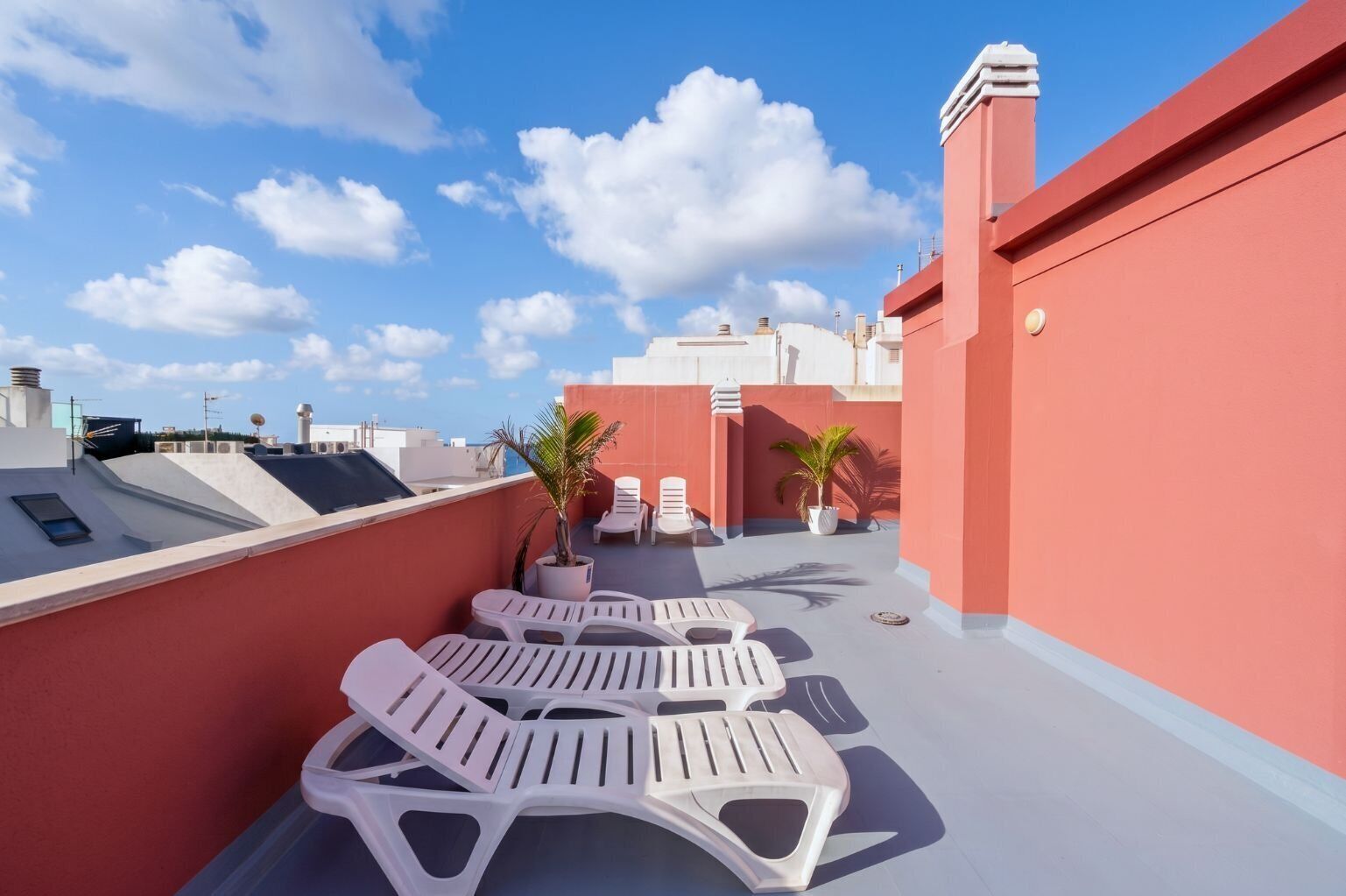 Eine Dachterrasse mit weißen Lounge-Stühlen, Topfpflanzen und blauem Himmel.