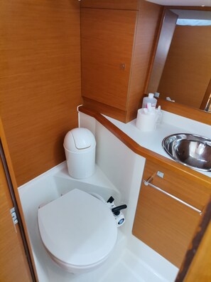 A compact bathroom with a white toilet, a small trash bin, a mirror, and a sink. - Sibenik Sun and Beach Sailing Extravaganza (Skradin)