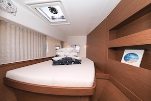 Une chambre à coucher compacte et moderne, dotée d’un lit aux lignes courbes, d’une lucarne, d’une tête de lit avec un ventilateur intégré et d’une étagère murale agrémentée d’un tableau.