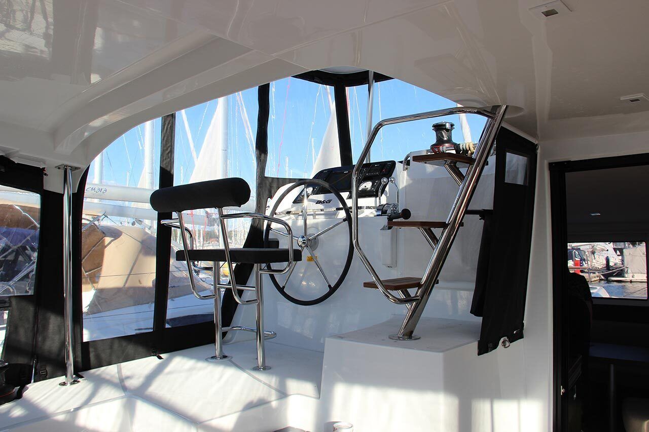 Interior de un barco con timón, panel de control y zona de estar.