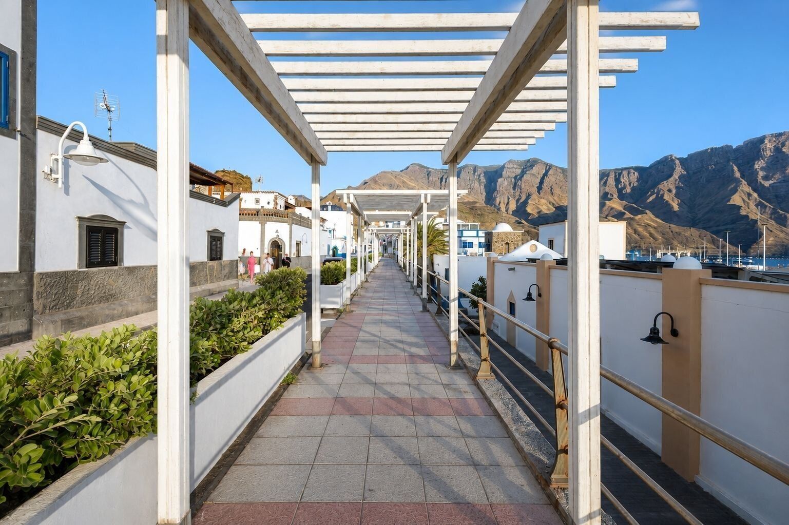 A covered walkway with white railings, leading to a building with a mountain backdrop.