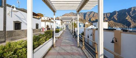 A covered walkway with white railings, leading to a building with a mountain backdrop.