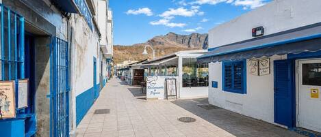 A narrow street with buildings on both sides, a sign for a restaurant, and a mountain in the background.