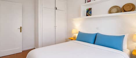 Una habitación de hotel con una cama, un armario, un estante con sombreros y una pared con cuadros.