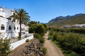 A white building with a palm tree, a dirt path, and mountains in the background. - GuestReady - Casa Carmen Terrace Sea View (Agaete)