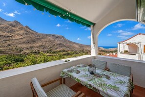 Ein Balkon mit Tisch und Stühlen, der auf eine gebirgige Landschaft und das Meer blickt.