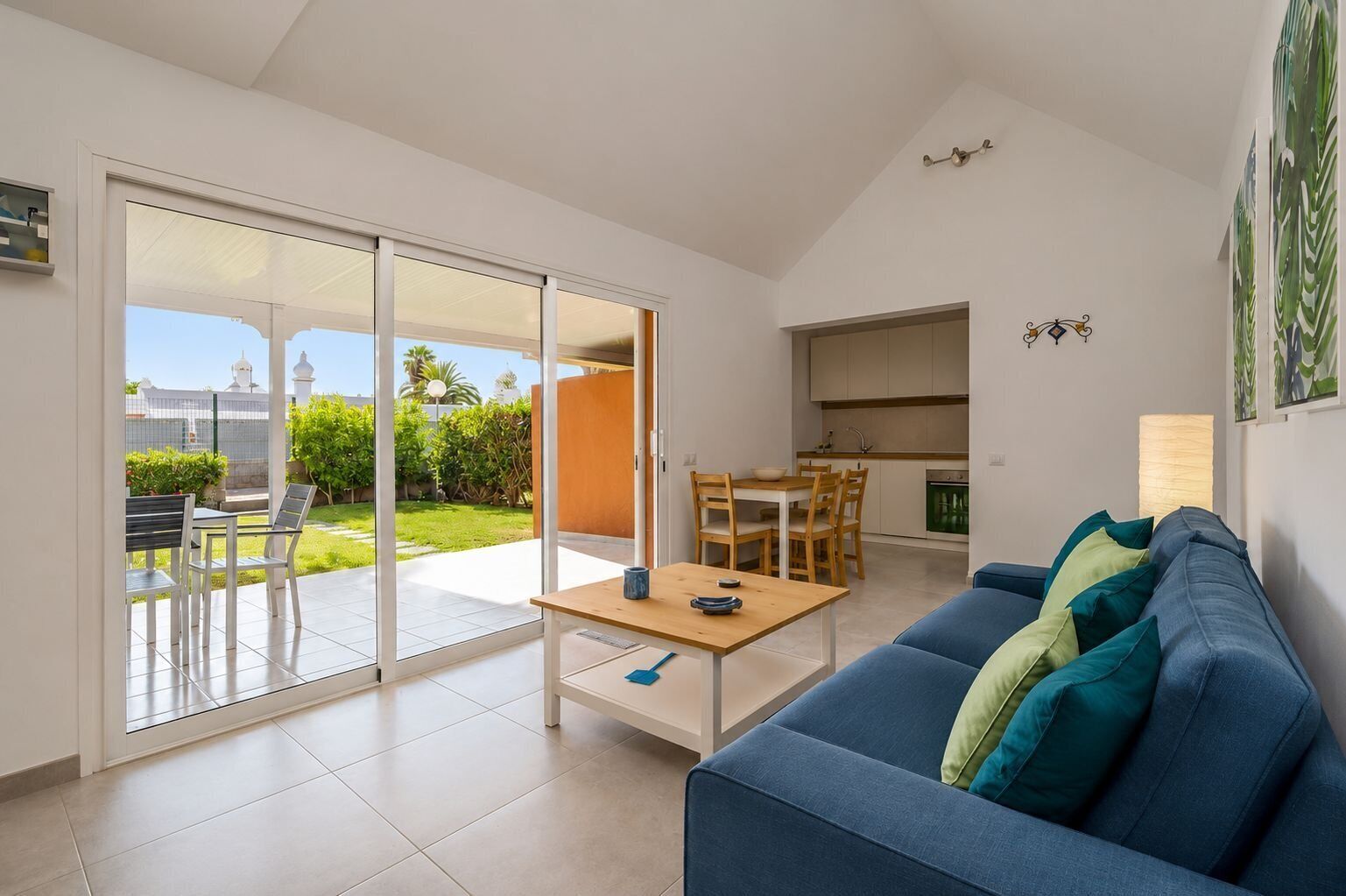 A modern living room with a blue sofa, a dining table, and a sliding glass door leading to a patio.