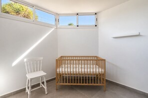 A room with a crib, a white chair, and a small window. - GuestReady - Melocotones Family Bungalow (San Bartolomé de Tirajana)